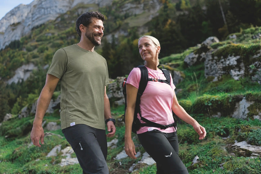 Paar beim Wandern in den Bergen, er im olivgrünen, sie im rosa Merino Shirt